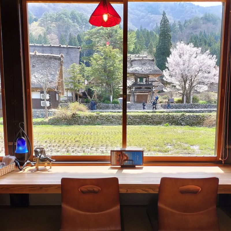 窓の外に満開の桜と合掌造りの家が見える窓辺の席