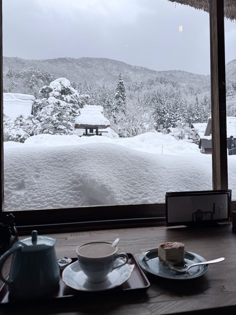 深い雪と白い茅葺き屋根を眺める窓辺のコーヒー