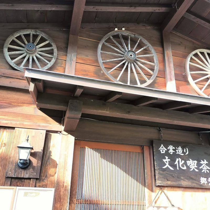 軒下に掛かる「合掌造り 文化喫茶」の看板と車輪の飾り