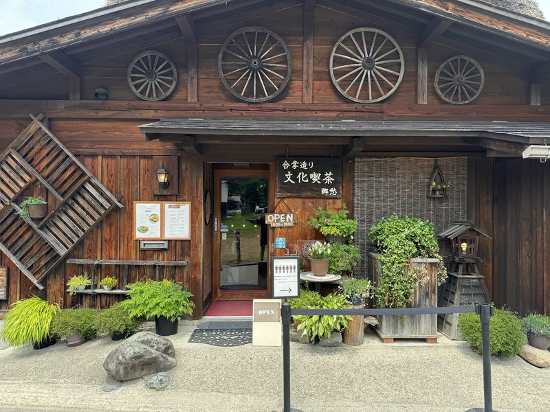車輪の飾りと鉢植えが並ぶ、木造の正面入口