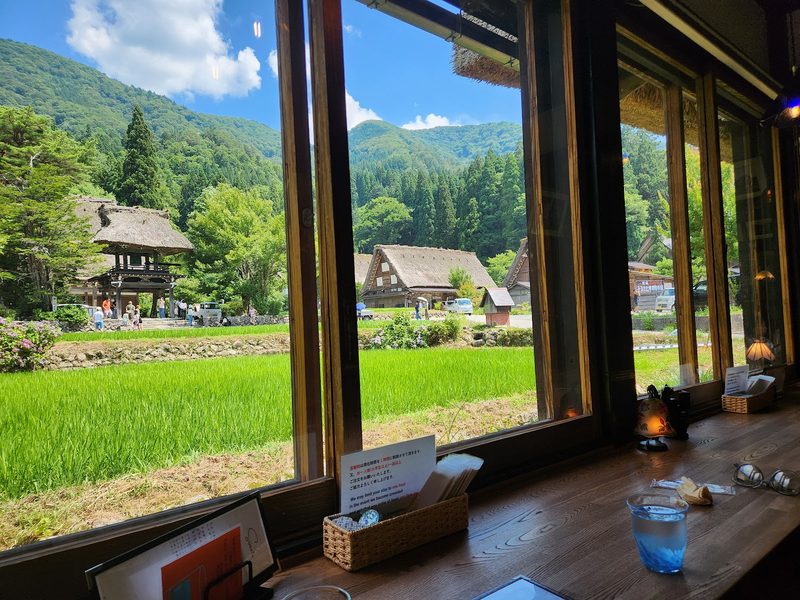 青々とした田んぼと合掌造りの家が見える窓辺