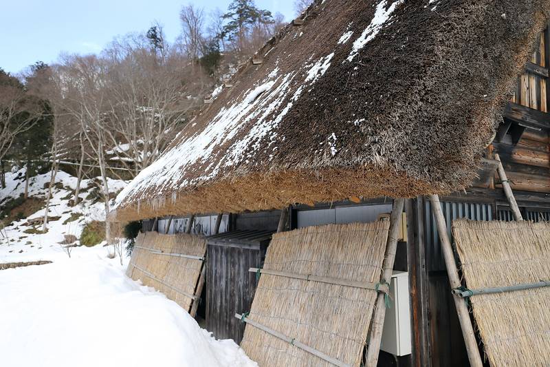 茅葺きの合掌造りの家に取り付けられた冬の雪囲い